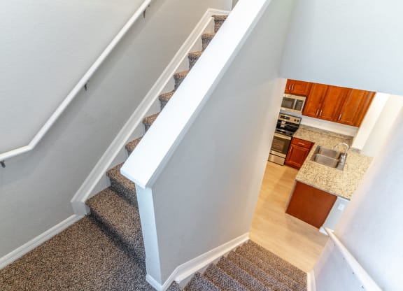 a view from the top of the stairs looking down into the kitchen and living room