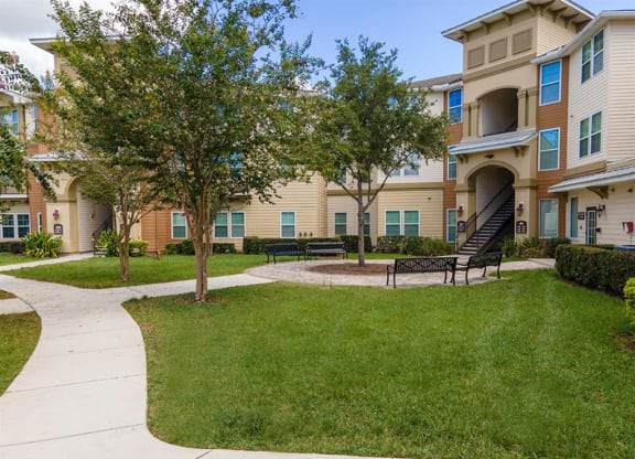 a grassy area with benches and trees in front of an apartment building