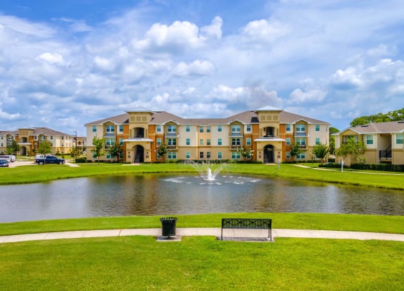 a fountain sits in the middle of a pond in front of an apartment complex