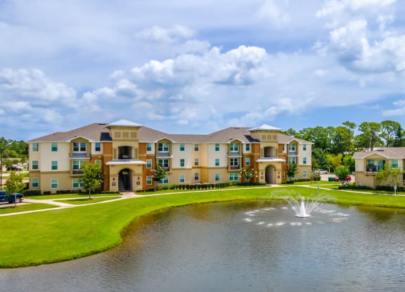 a fountain sits in the middle of a pond in front of an apartment complex