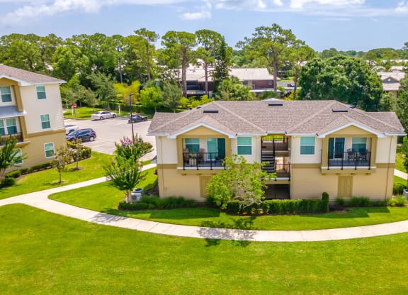an aerial view of an apartment with a green lawn and trees in the background