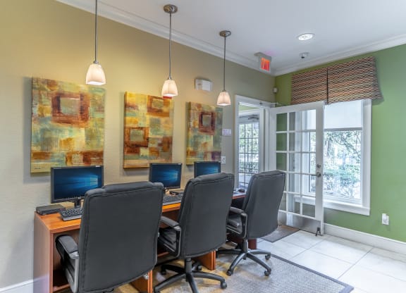 a desk with four computers in a room with green walls and a glass door