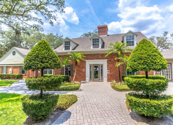 a house with a brick exterior and a brick pathway with trees and bushes on either side