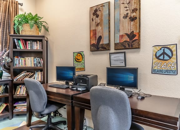 a desk with two computer monitors and two chairs in a room with a bookshelf and
