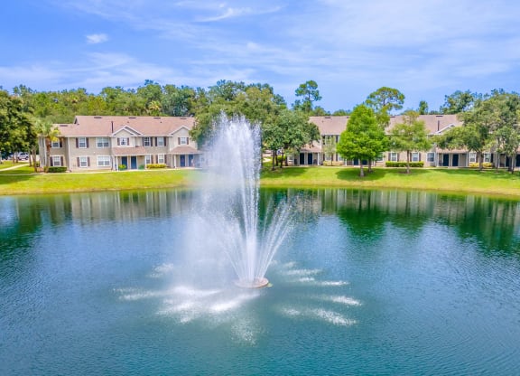 a fountain in the middle of a pond with apartment buildings in the background