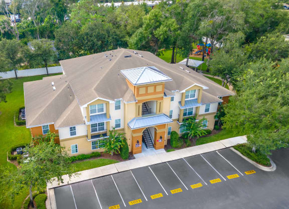 an aerial view of a large yellow house with a parking lot and trees