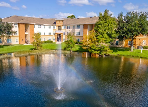 a fountain sits in the middle of a pond in front of a building