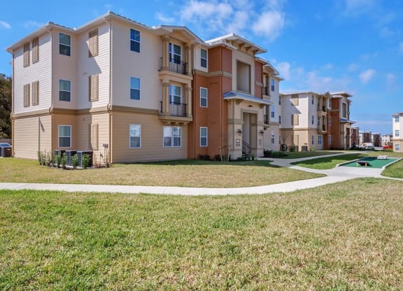 a row of apartment buildings with a sidewalk and grass