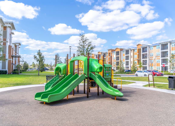 a playground with a green slide in front of an apartment complex