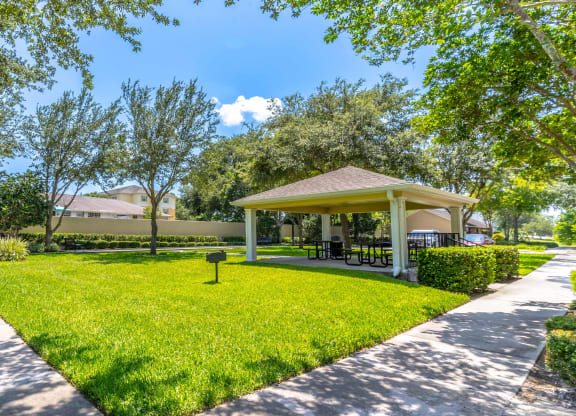 a pavilion with a picnic table and grill in the middle of a grassy area with