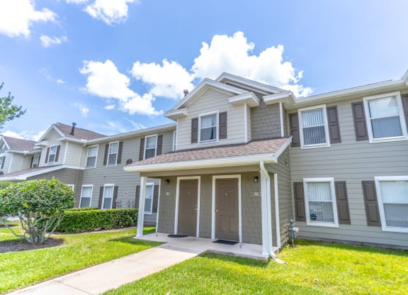 an apartment building with a grassy yard and a blue sky in the background