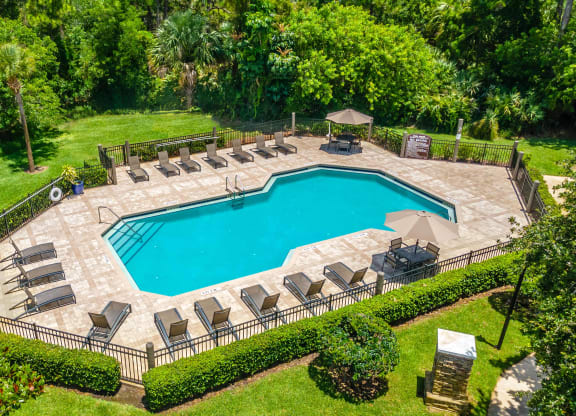 an aerial view of a backyard pool with lounge chairs and a manicured lawn