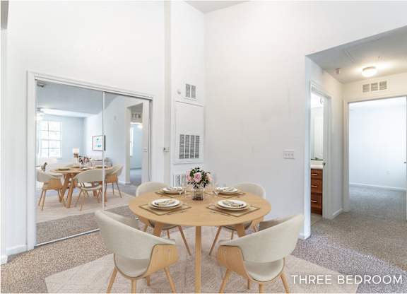 A dining room with a table set for six with a view of the kitchen.
