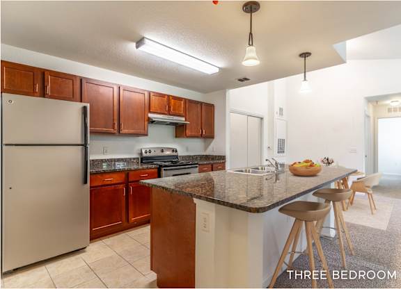 A kitchen with a refrigerator, stove, and bar stools.