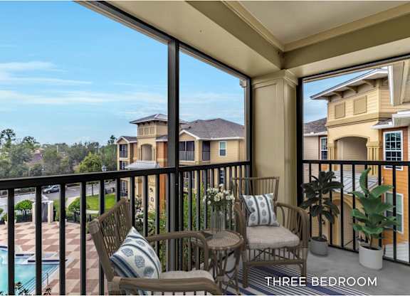 A balcony with chairs and a table overlooking a pool and houses.