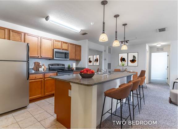 A kitchen with a refrigerator, microwave, and a counter with chairs.