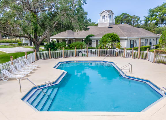a swimming pool with chaise lounge chairs and a house in the background