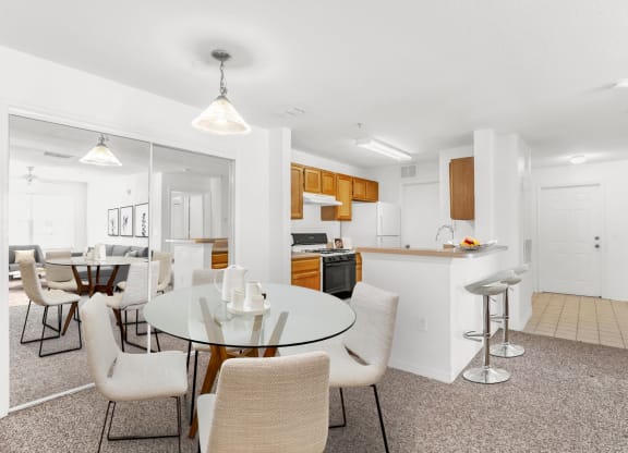 a dining area with a glass table and chairs and a kitchen in the background
