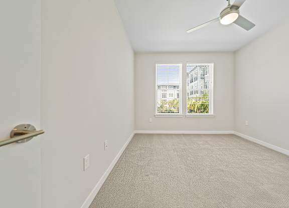 A room with a ceiling fan and a window with a view of a building.