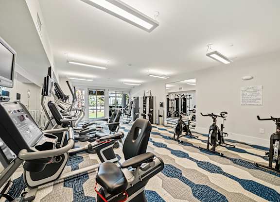 A gym with a variety of exercise equipment including treadmills, stationary bikes, and weight machines.