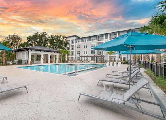 A pool area with sun loungers and a building in the background.