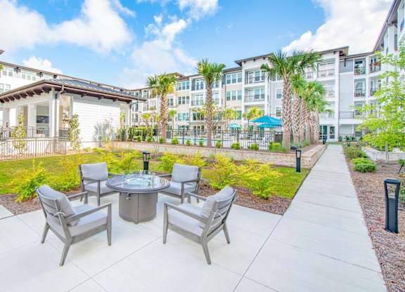 A patio with a table and chairs is surrounded by a grassy area and buildings.