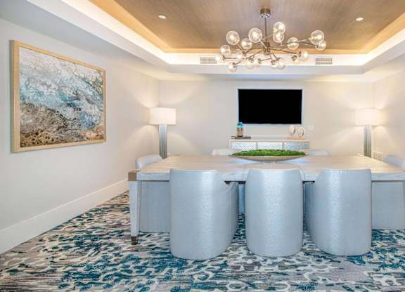 A room with a large table and chairs with a painting on the wall.