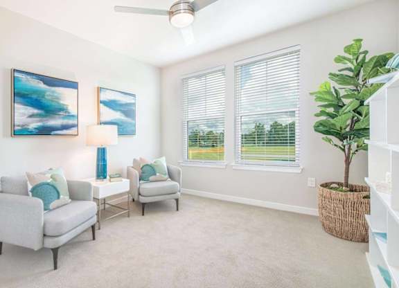 A living room with two grey couches, a ceiling fan, and two paintings on the wall.