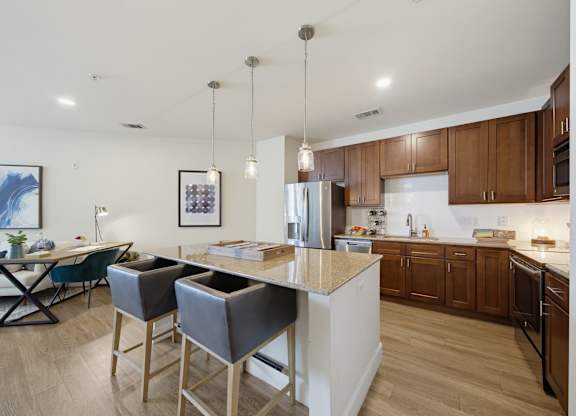 Kitchen with an island seating two, stainless steel appliances, dark wood cabinets, pendant lights, and a tile backsplash.