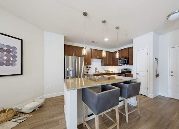 Kitchen island with two bar stools, a stainless refrigerator and range, dark wood cabinets, and three pendant lights.