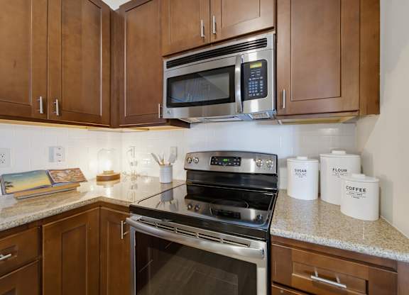 Stainless steel electric range and over-range microwave set against a white subway tile backsplash and wood cabinets.