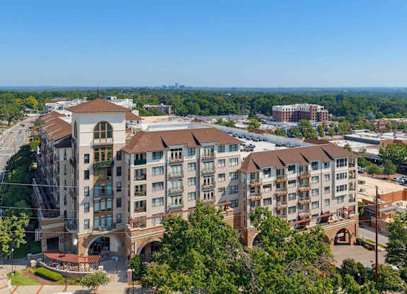 Aerial of the apartment building's central tower and arched windows, with the distant Raleigh skyline on the horizon.