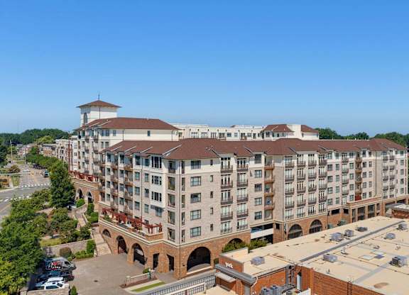 Aerial of the apartment building's roofline and balconies, with the arched brick arcade and parking at street level.