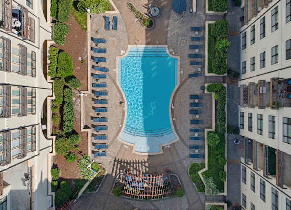 Overhead view of the pool courtyard, with lounge chairs lining both sides and hedges between the building wings.