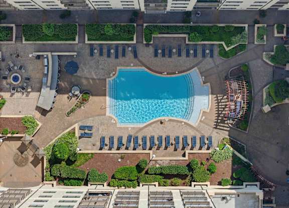 Overhead view of the pool deck, with two rows of loungers, a shaded seating area, and a fire pit at the near corner.