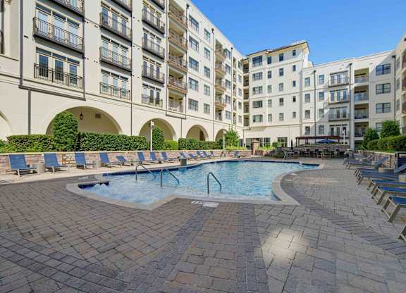 Pool and spa at The Clark at Village District, edged by a paver deck, loungers, and arched breezeways under the homes.