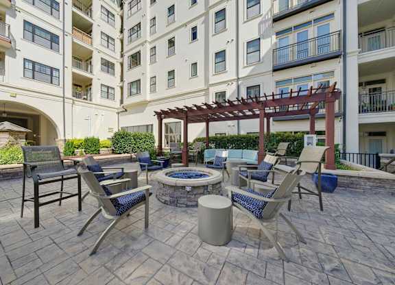 Courtyard fire pit with blue fire glass, sling chairs around it, and a pergola with sectional seating set beyond.