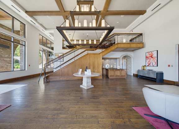 Clubhouse lobby with exposed beams, a large iron chandelier, a wood staircase, and tall windows onto the arcade.
