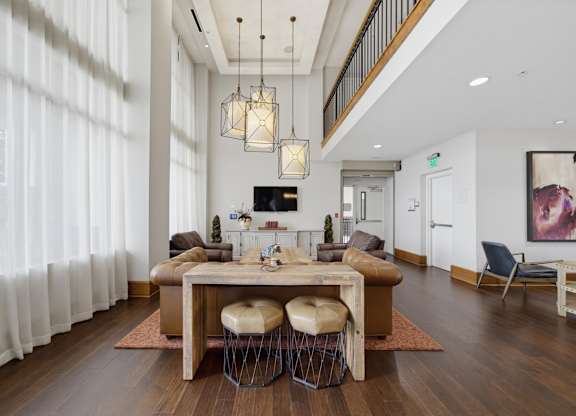 Double-height resident lounge with lantern pendants, soft seating, a long wood table, and floor-length curtains.