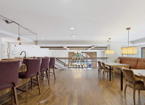 Upper-level bar with stools, dining tables along a long bench, pendant lighting, and a railing over the lobby below.