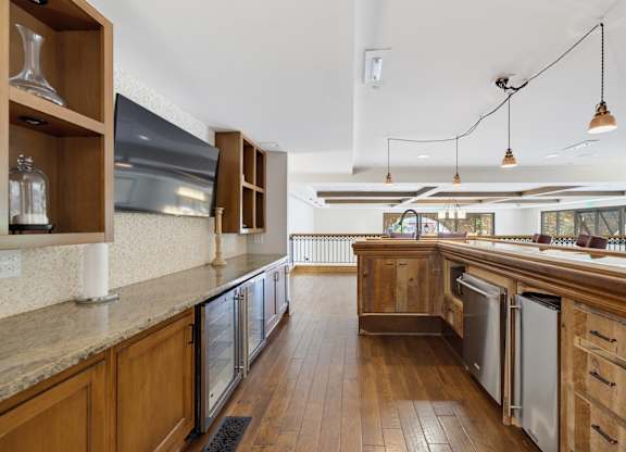 Resident bar with a long counter, glass-front beverage refrigerators, a mounted screen, and a reclaimed wood island.