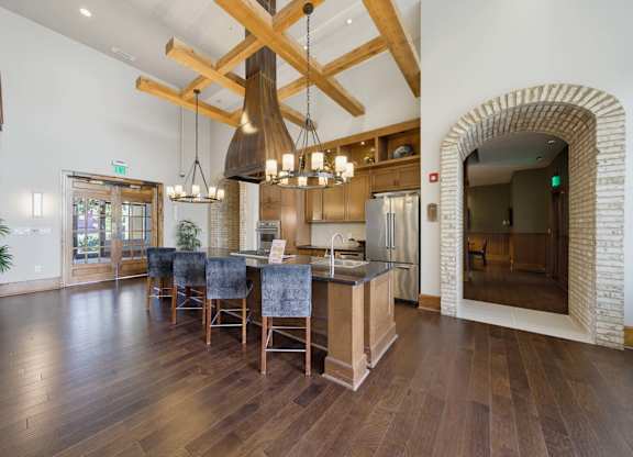 Resident kitchen under timber beams, with a tall vent hood, an island seating four, wall ovens, and a stainless fridge.