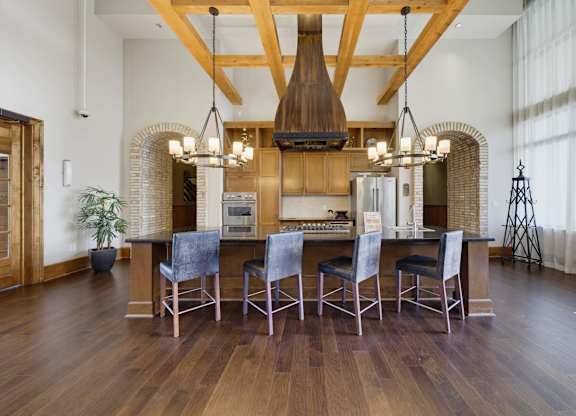 Resident kitchen island with a gas cooktop and four stools, flanked by brick archways under two iron chandeliers.