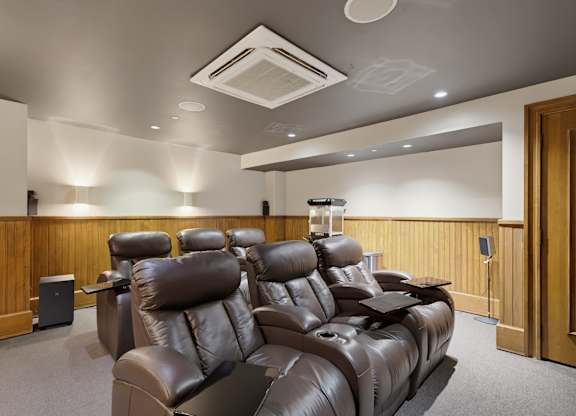 Theater room with two tiered rows of reclining seats, fold-out tray tables, wall sconces, and a popcorn machine.