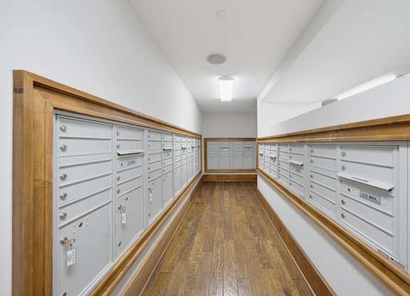 Mailroom lined with resident mailboxes on both walls, wood trim and a hardwood floor, lit from overhead fixtures.