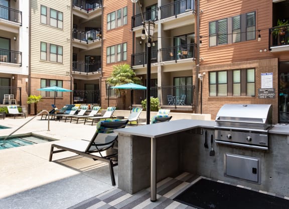 an outdoor kitchen with a grill and lounge chairs in front of an apartment building
