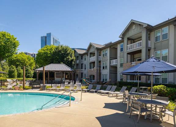 A pool area with chairs and umbrellas in front of apartment buildings.