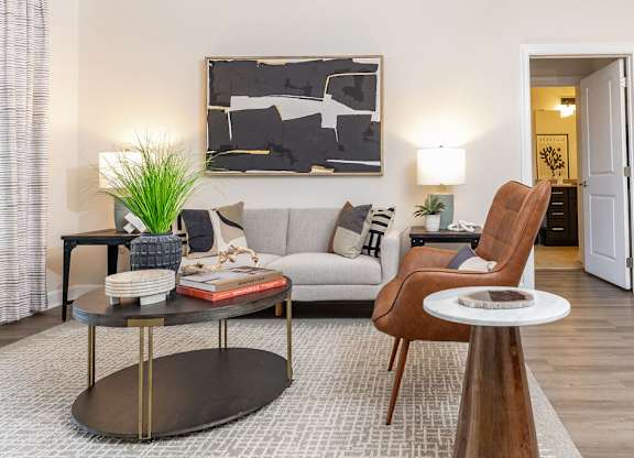 A living room with a grey couch, a wooden chair, a coffee table, and a painting on the wall.