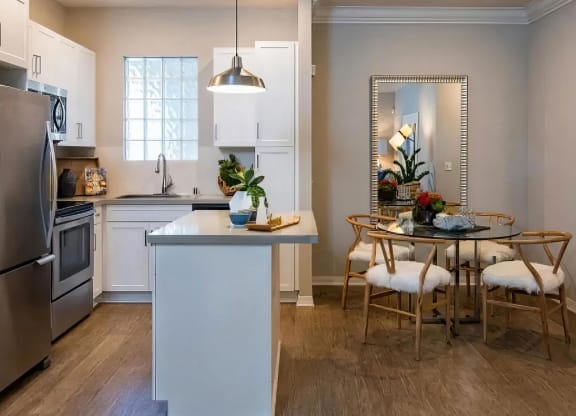 Kitchen with white cabinets and a peninsula island, opening to a dining area with a glass table and four chairs.