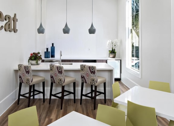 Shared kitchen counter with three cushioned bar stools, a sink, and green-chaired cafe tables along the window.